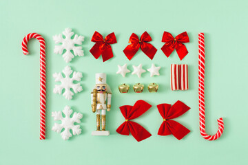 Christmas composition on a mint green background. White, red and gold decorations. Christmas, winter, new year concept. Nutcracker, bow, ribbon, candy cane, stars and balls. Minimal creative concept.