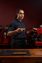 Portrait of a handsome barista in black shirt and apron at the bar of the modern cafe.