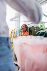 joyful african american woman pointing at blurred pink dress near friend