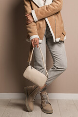 Fashionable woman with stylish bag near beige wall, closeup