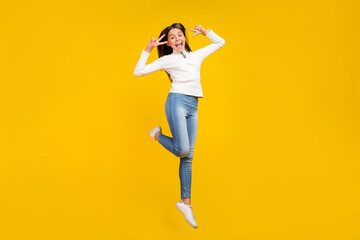 Full size photo of sweet brunette little girl jump show v-sign wear pullover jeans footwear isolated on yellow color background