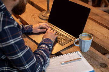 Cropped image of young man chatting via net-book during work break in coffee shop, male sitting in...