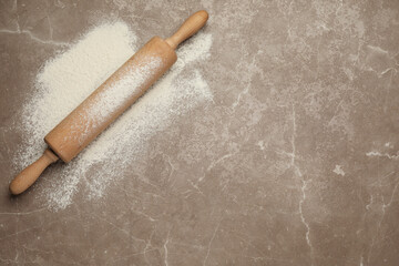 Wooden rolling pin and flour on grey background, top view. Space for text