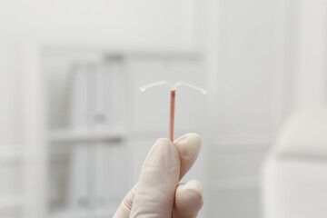 Doctor holding T-shaped intrauterine birth control device on blurred background, closeup - obrazy, fototapety, plakaty