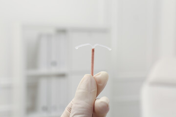 Doctor holding T-shaped intrauterine birth control device on blurred background, closeup