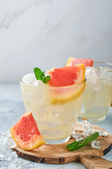 Lemonade drink made from grapefruit, soda water and mint leaves with ice on light blue slate, stone or concrete background. Healthy homemade lemonade or cocktail. Mock up. Top view.
