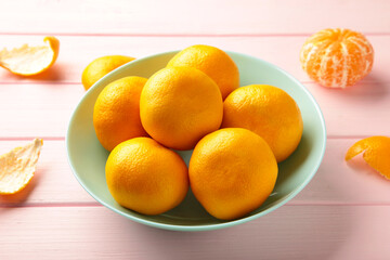Fresh mandarin oranges fruit on mint bowl on pink wooden background.