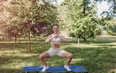 a young girl in white sportswear is doing fitness outdoors in the park