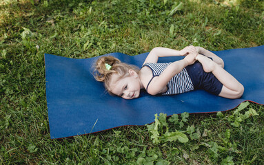 a little girl does yoga lying on a sports mat in the park