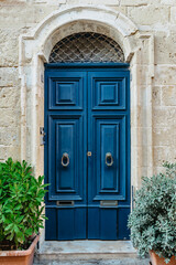 Obraz na płótnie Canvas Malta is home to amazingly unique doors.Traditional colorful Maltese door in Valletta.Front door to house from Malta.Blue wooden door and stone facade with plants.Maltese vintage apartment building.
