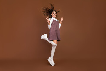 Full length photo of young cheerful girl show fingers peace cool v-symbol footwear isolated over brown color background