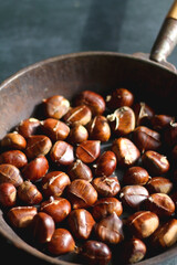 Pan filled with chestnuts on dark background. Selective focus.