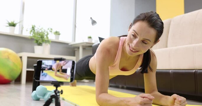 Young woman doing physical exercises, standing on board on mat taking pictures on camera slow motion 4k movie