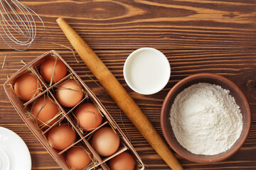 Ingredients for baking - flour, eggs, milk. With rolling pin, whip and pouch. On wooden table