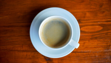 Obraz premium a cup of coffee on the white saucer. a morning coffee served on the wooden table from the top view. a shot of beverage object suitable for background or promotion.