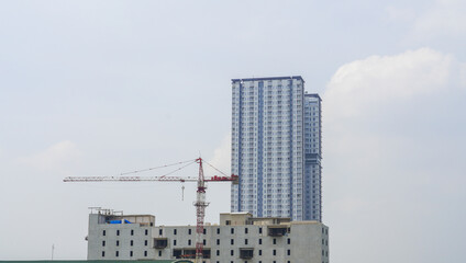 the high-rise building with a building construction beside. under-construction building with a crane operates. the view of the skyscraper development in the city.