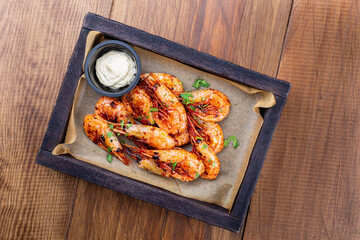 Grilled shrimps or prawns served with white sauce on a wooden tray, wood brown background. Seafood. Top view. Flat lay