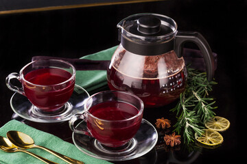 Fruit red tea with berries in glass teapot and two glass cups on black background