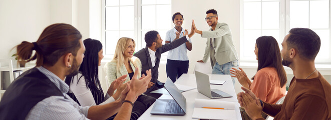 Fototapeta Mixed race business team celebrating good results in office meeting. Happy young black man gives high five to coworker while diverse multi ethnic teammates are applauding. Teamwork and success concept obraz