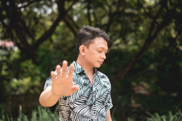A young asian man refuses to cooperate, extending his hand out to make a stop gesture while looking...