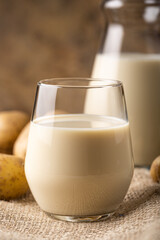 Vegan potato milk in glass and potato on brown background, close up. Plant based milk replacer and lactose free concept with copy space