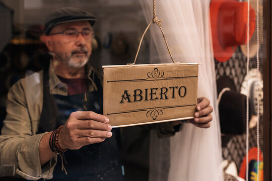 Mature male seller hanging shop open sign in fashion boutique