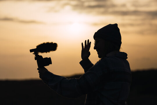 Anonymous happy lady recording vlog on camera under sundown sky