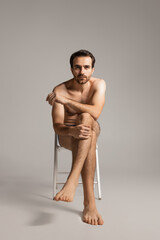 Fototapeta na wymiar Portrait of young handsome bearded shirtless man sitting on chair isolated on white studio background. Natural beauty