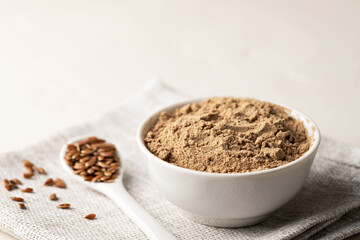 Flaxseed flour in a bowl and flax seeds on a light background. Selective focus. Close-up, copy space
