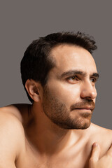 Close-up portrait of young handsome bearded shirtless man isolated on gray studio background. Natural beauty