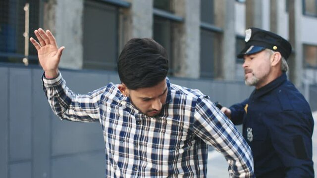 Cinematic police arrest with criminal led away in handcuffs. Policeman preparing to puts the handcuffs on the hands of criminal