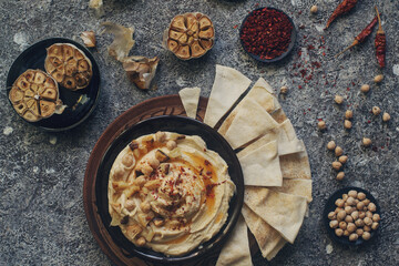 Traditional homemade middle eastern dish - hummus decorated with chickpeas, garlic, olive oil and spices on dark stone table