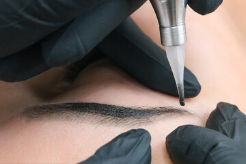Naklejka premium Beautician makes permanent eyebrow makeup on the face of a beautiful young woman.