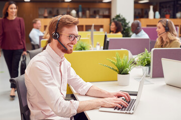 Businessman Wearing Headset Talking To Caller In Busy Customer Services Centre