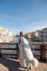 Woman hugs her dog while standing on the Academy bridge, enjoying great view on famous Grand Canal...