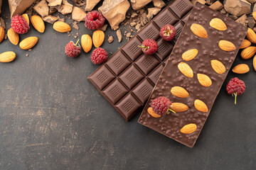 Cooking chocolate bars with almonds, raspberries, handmade sweets. Composition of bars and pieces of dark almond chocolate, raspberries on a black background, top view. Pastry craft on the table