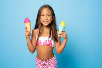 Cute little girl wearing swimsuit holding ice cream isolated over blue background.