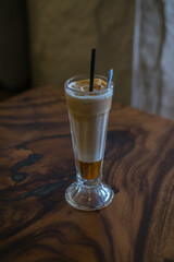 Close-up photo of glass cup with ice latte on the wooden table in a coffee shop. Glass with iced caramel cappuccino with the straw on the table
