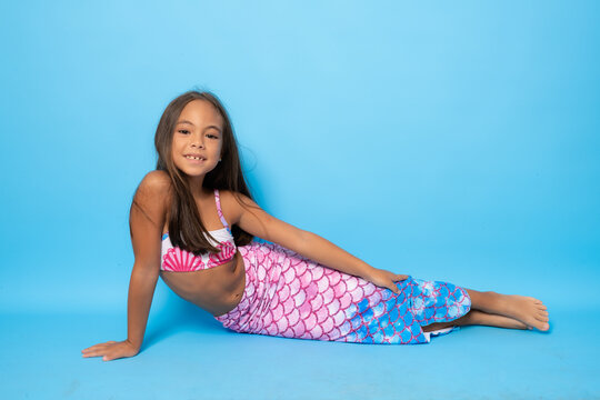 Cheerful little girl wearing swimsuit lying on floor isolated over blue background.