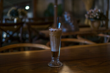 Close-up photo of glass cup with ice latte on the wooden table in a coffee shop. Glass with iced caramel cappuccino with the straw on the table
