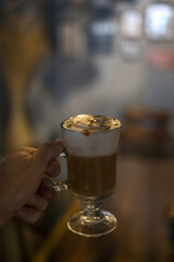 Close-up photo of glass cup with latte in the coffee shop. Hand holding the glass with caramel cappuccino in the restaurant. Photo for the menu