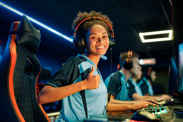 Happy female gamer showing thumb up sign and smiling while using powerful computer for online game...
