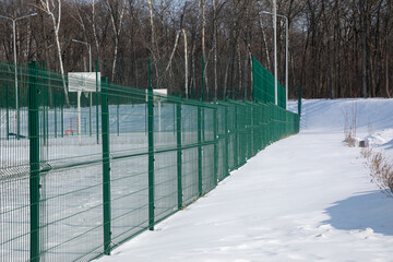 green mesh metal fence encloses children's playground in winter. Sectional fencing installation