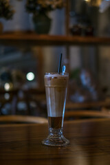 Close-up photo of glass cup with ice latte on the wooden table in a coffee shop. Glass with iced caramel cappuccino with the straw on the table