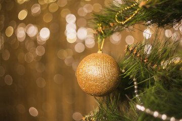 Golden Christmas toys, balls, garlands on a spruce branch on a shiny background with bokeh