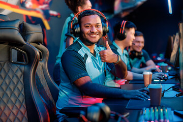Happy young man expressing satisfaction with game while giving thumbs up gesture during participation in international gaming event in gaming club