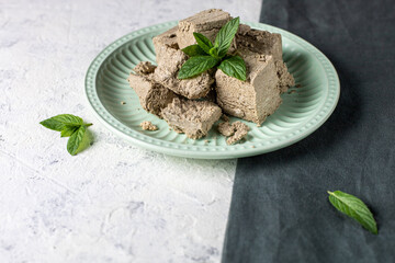 Pieces of halva on green plate. Sweet dessert with mint leaves on white background