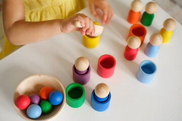 Child throws a yellow ball into a cup of the appropriate color with a spoon. Educational game -...