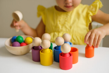 Obraz premium Wooden colored toy for learning colors and developing logic of preschoolers. A child plays at a table in the children's room with cups, balls and cylinders. Preschool education
