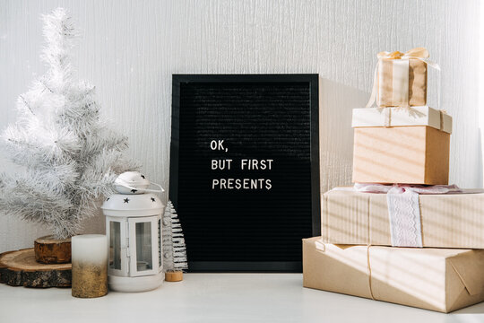 Many craft Christmas gift boxes and black letter board with quote Ok but first presents. Festive Christmas letter board ideas and quotes. Blackboard with the Xmas phrase on table